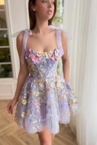 A close-up of a Lavender Floral Lace Mini Prom Dress with intricate multicolored floral embroidery and delicate shoulder tie straps. The dress features a sweetheart neckline and a flowy skirt.